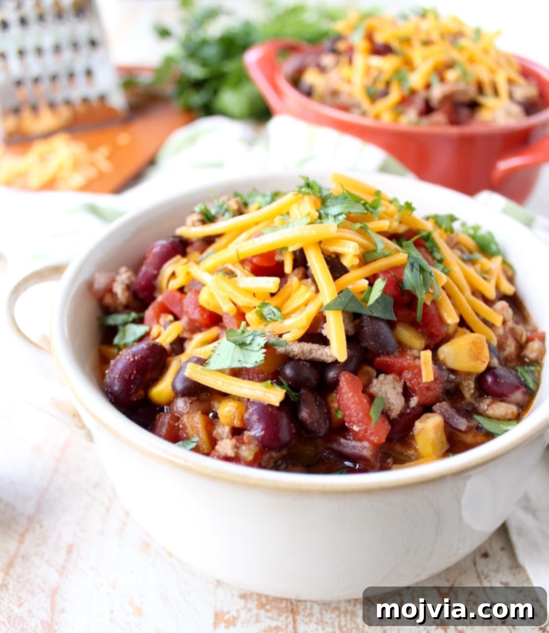 One-Pan Fiesta Turkey Soup 3 A white bowl filled with taco soup topped with shredded cheese and herbs.