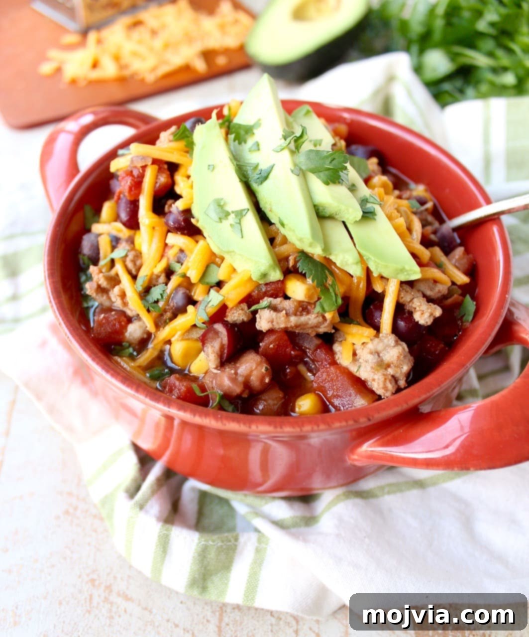 One-Pan Fiesta Turkey Soup 4 A red bowl filled with turkey taco soup topped with shredded cheese and avocado.