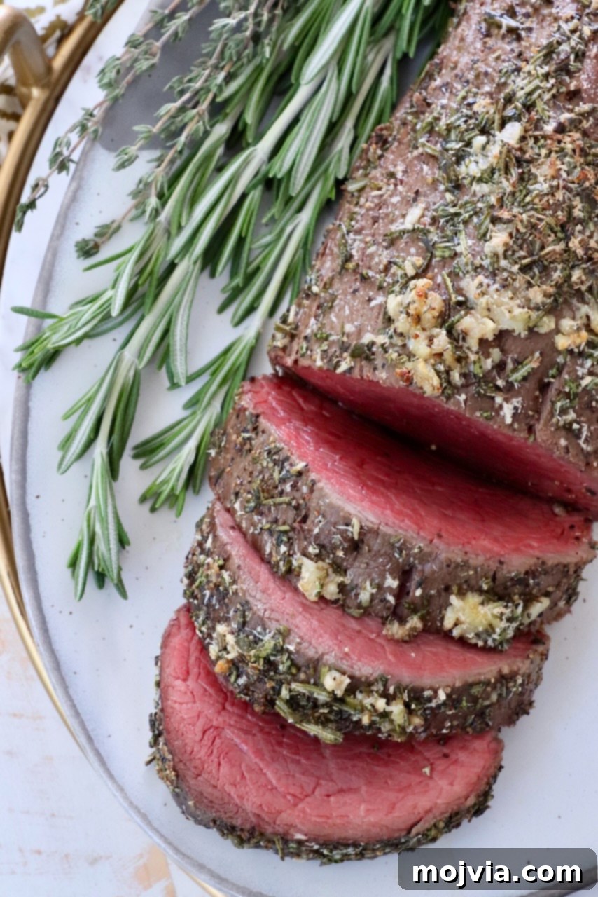 Sliced herb crusted beef tenderloin on a platter with fresh herbs, ready to serve.
