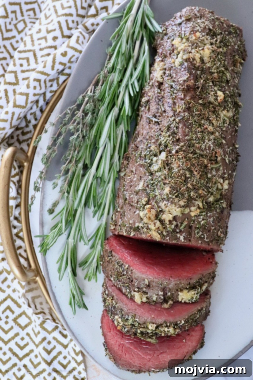 Herb crusted beef tenderloin on a plate, garnished with fresh herbs, ready for serving.