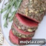Sliced beef tenderloin on a plate with fresh rosemary garnish.