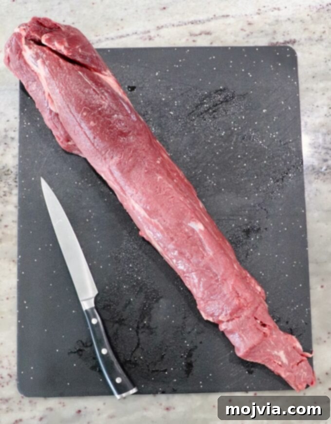 A whole beef tenderloin resting on a cutting board next to a sharp knife.
