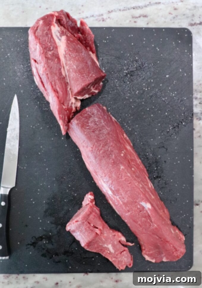 A beef tenderloin expertly cut into three distinct sections on a cutting board, with a knife nearby.