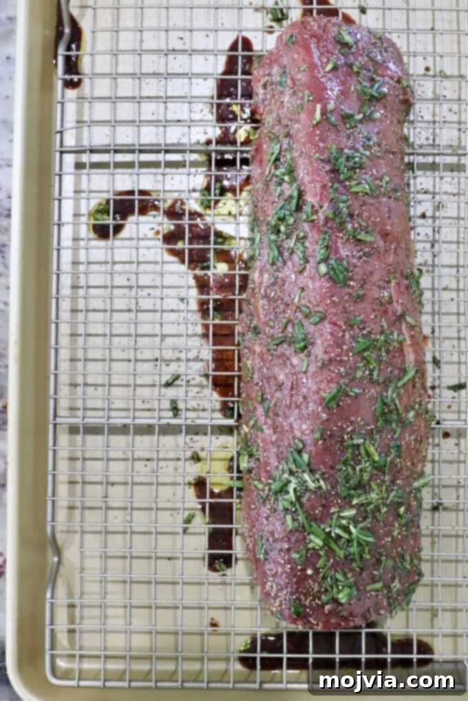 Herb rubbed beef tenderloin on a wire rack above a rimmed baking sheet, showcasing the rich seasoning.