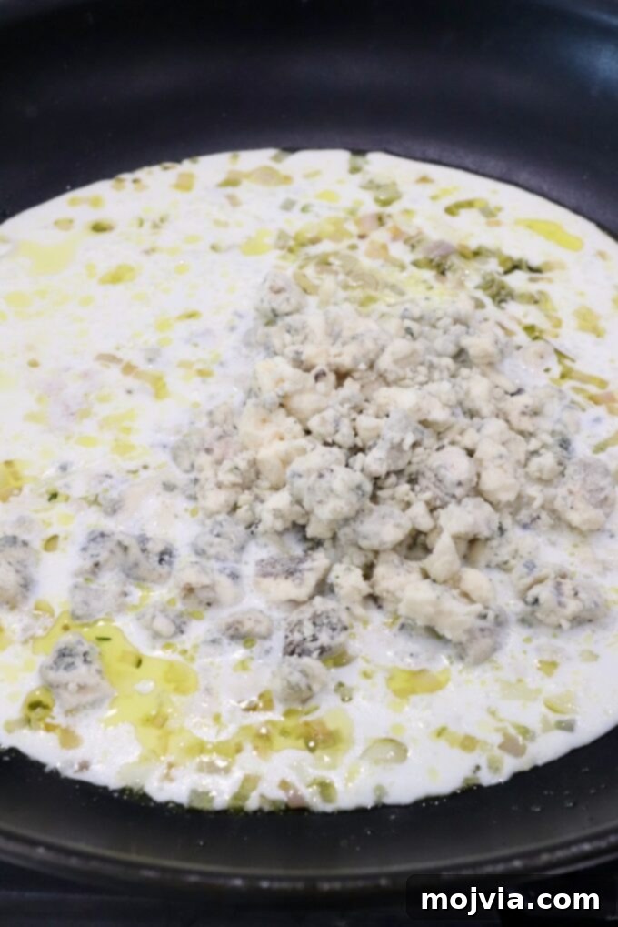 Gorgonzola crumbles melting into a rich cream sauce in a skillet on the stovetop.