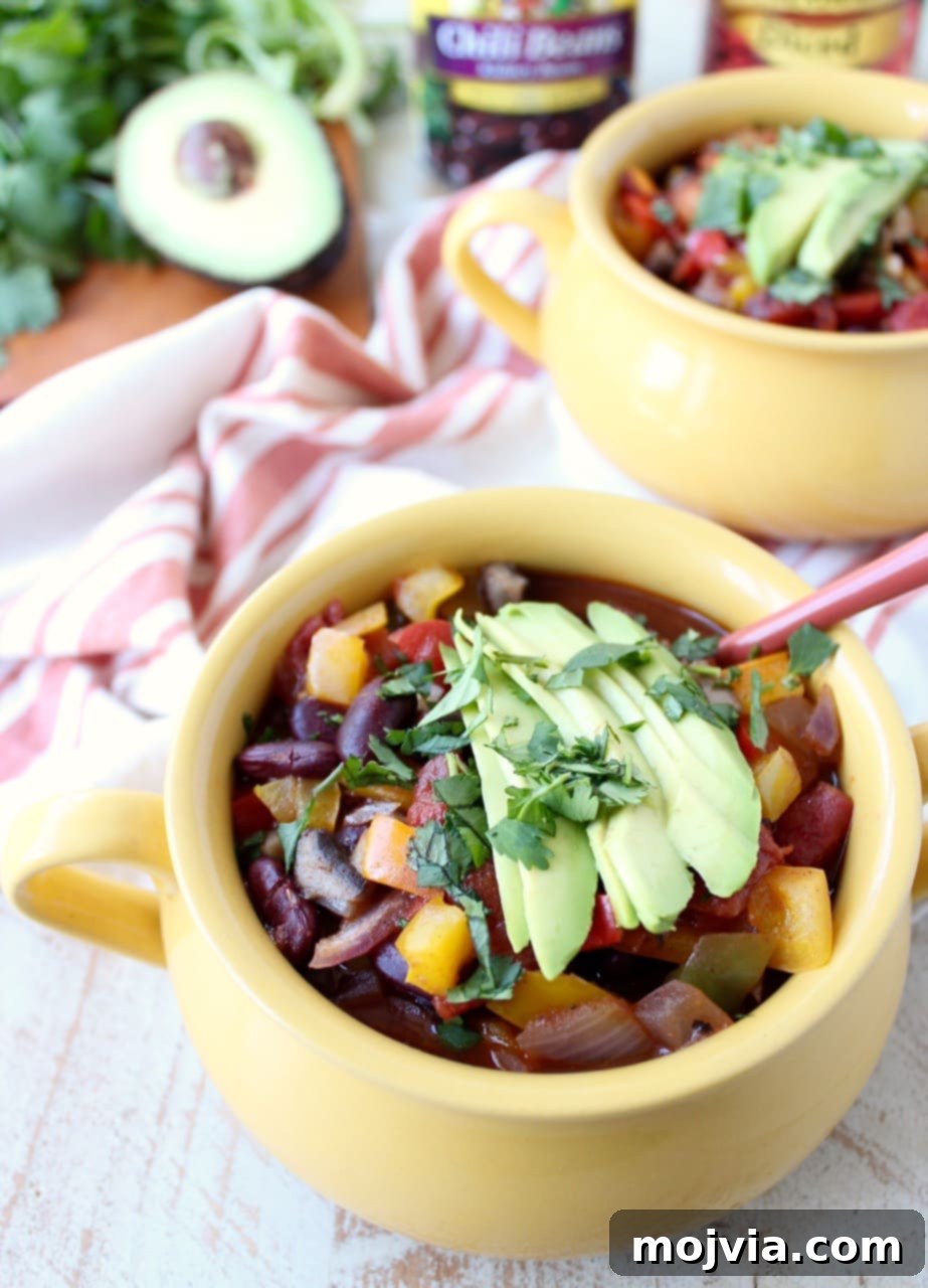 Close-up shot of the vegetarian chili in yellow crocks, garnished with delicate slices of avocado and a generous sprinkle of fresh chopped cilantro, highlighting its colorful and appealing texture.