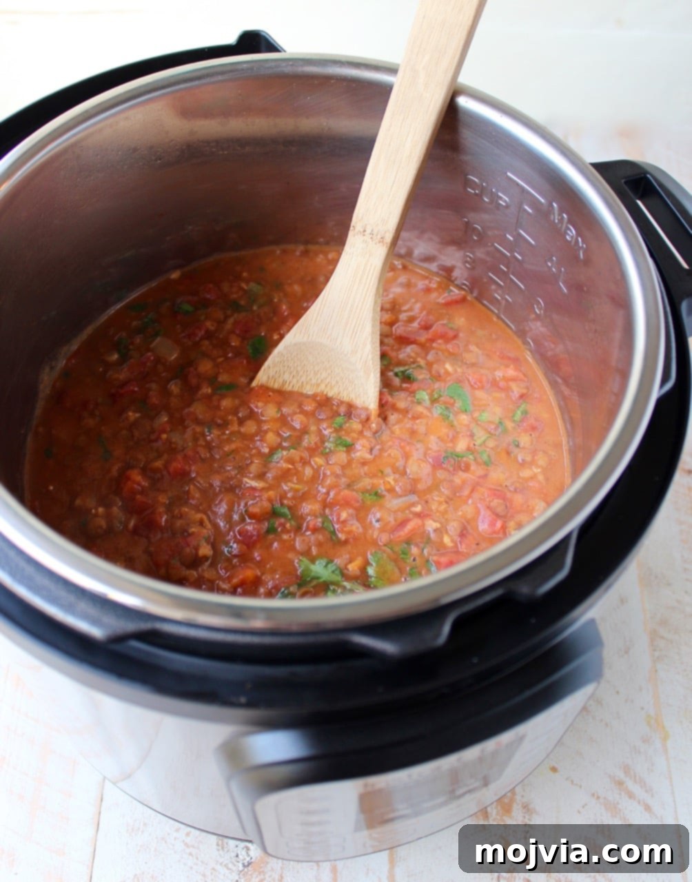 Instant Pot Tikka Masala Chicken and Lentil Bowls 3 A wooden spoon stirring chicken and lentils in a vibrant tikka masala sauce inside an Instant Pot.
