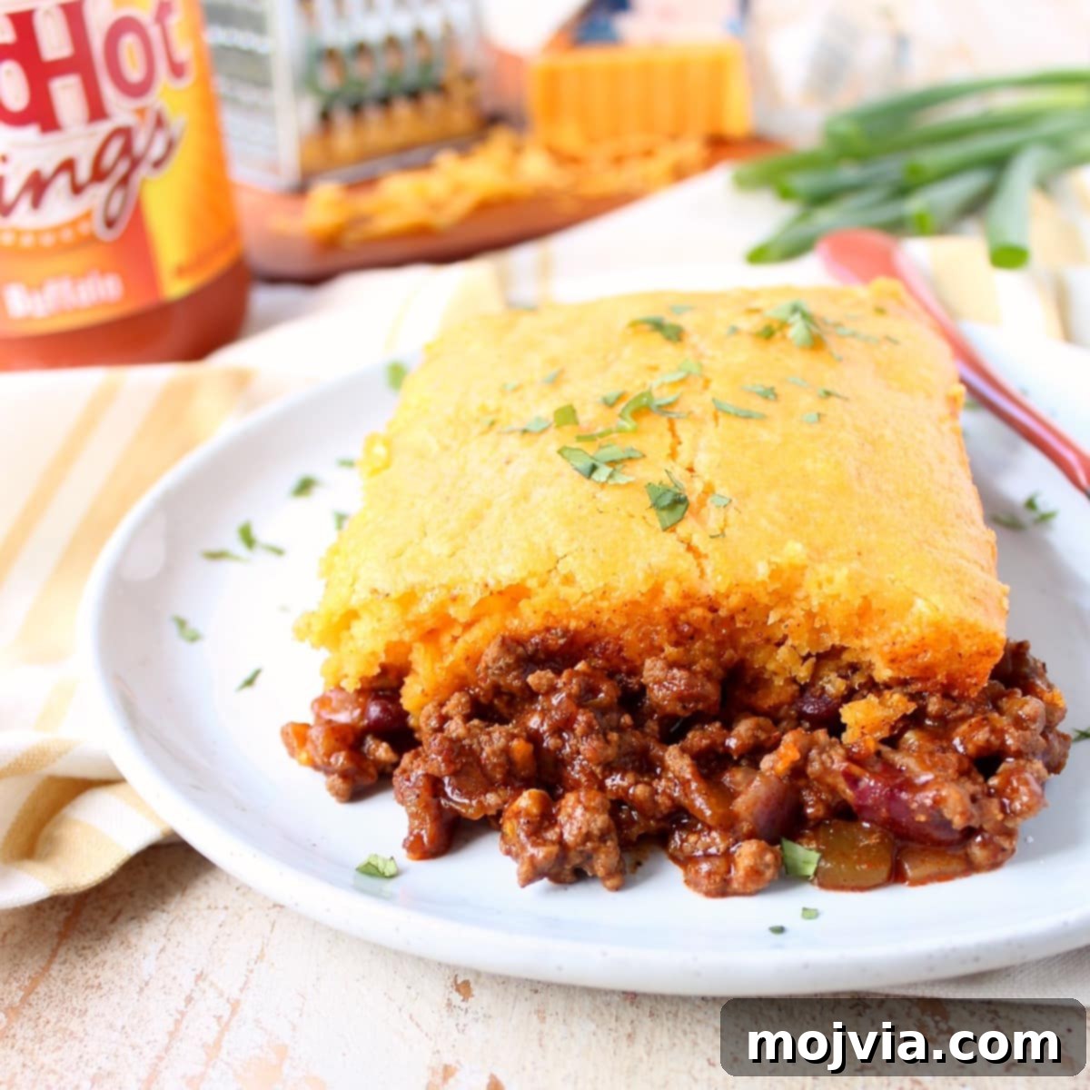 Cheesy Buffalo Chili Cornbread Bake 2 A generous slice of Buffalo Cheddar Cornbread Chili Pie on a white plate with a fork, showing layers of rich chili and golden cornbread.