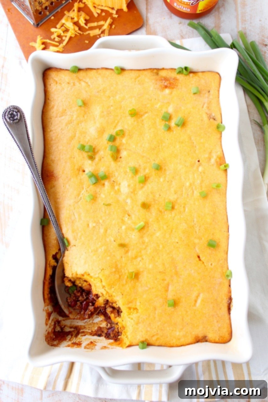 Cheesy Buffalo Chili Cornbread Bake 3 Hearty Buffalo Cheddar Cornbread Chili Pie in a casserole dish, ready to be served with a large serving spoon.