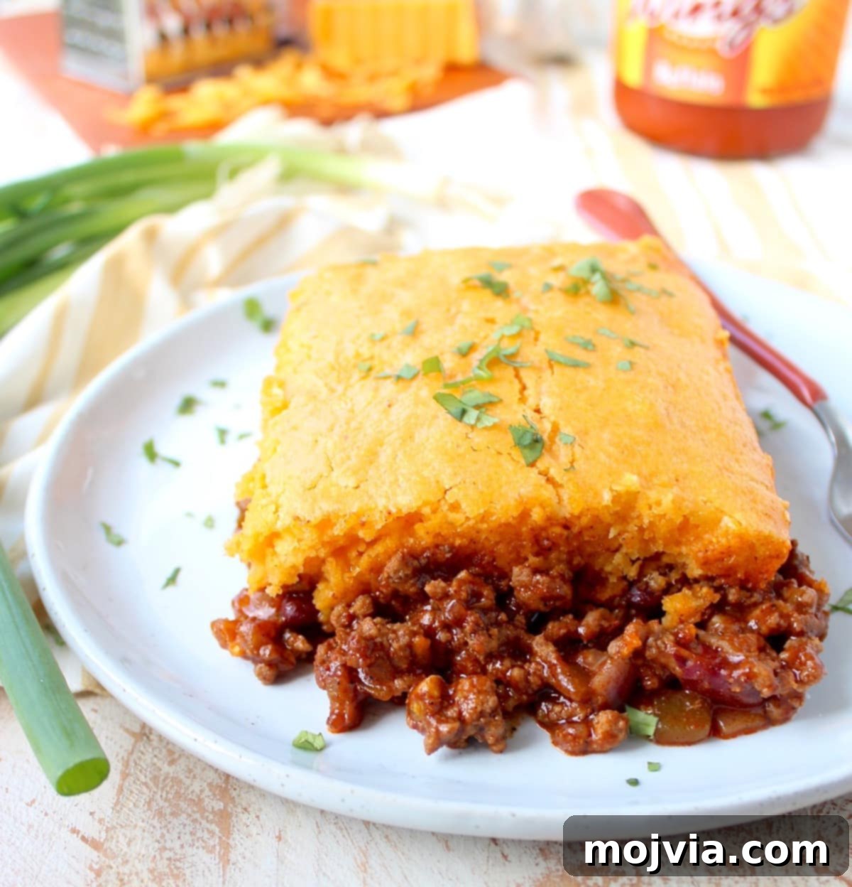 Cheesy Buffalo Chili Cornbread Bake 7 A perfectly baked piece of Buffalo Cheddar Cornbread Chili Pie, showcasing the golden-brown cornbread crust and the rich, bubbling chili underneath, served on a white plate.