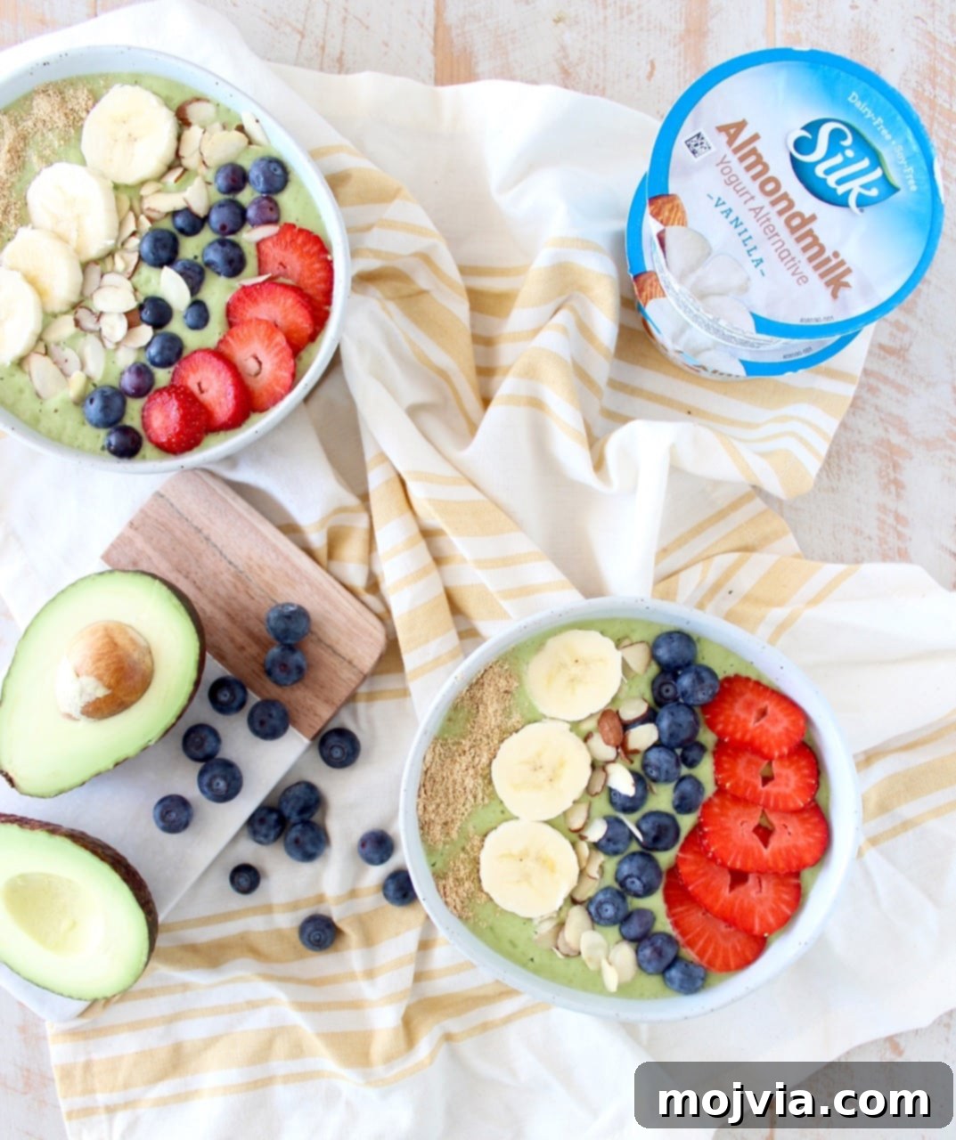 Close-up of a single green avocado smoothie bowl adorned with colorful fresh fruit toppings like sliced banana, berries, and chia seeds.
