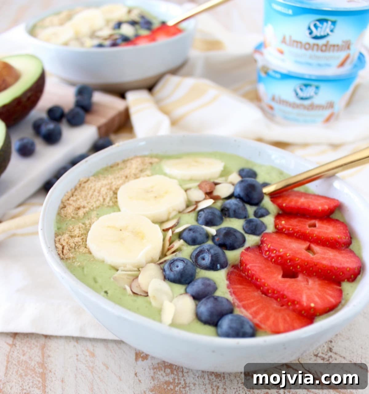 A beautifully presented green avocado smoothie bowl, garnished with colorful fresh berries, banana slices, and a sprinkle of seeds, ready to be enjoyed.