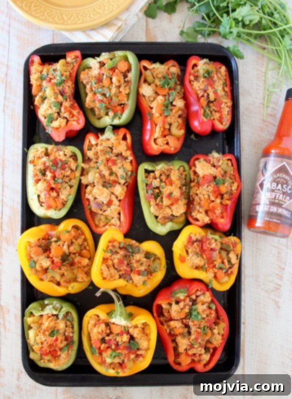 An overhead view of two Buffalo Chicken Stuffed Bell Peppers on a baking sheet, with a bottle of Tabasco Buffalo Sauce nearby, highlighting the key ingredient.