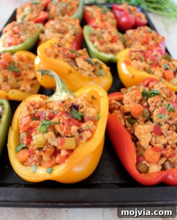 A baking sheet filled with cooked ground chicken, carrots, and celery mixture, perfectly stuffed into vibrant bell pepper halves, ready for the oven.