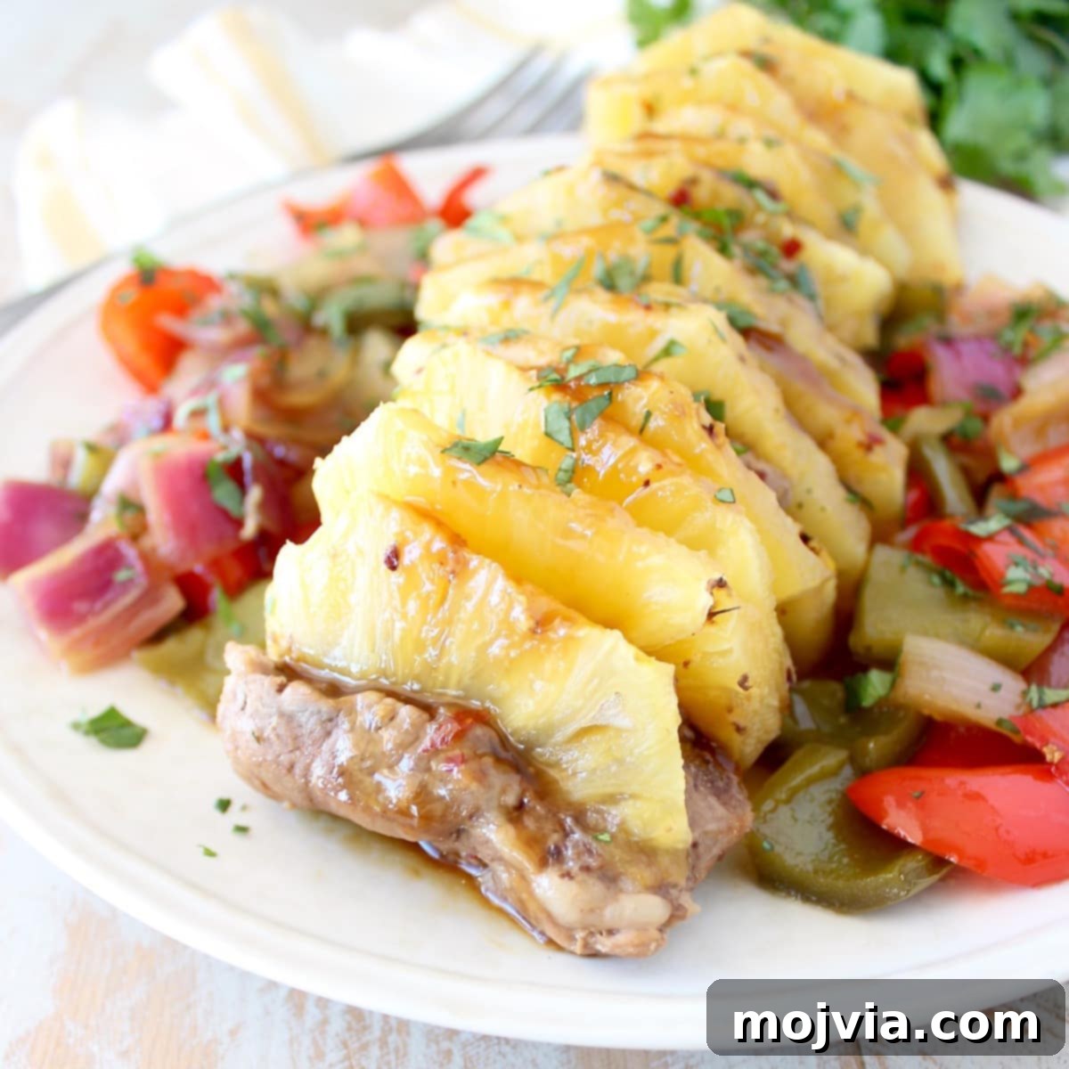 Sweet and Tangy Pineapple Teriyaki Pork Tenderloin 2 cooked pork tenderloin stuffed with slices of pineapple on a plate with diced bell peppers and onions