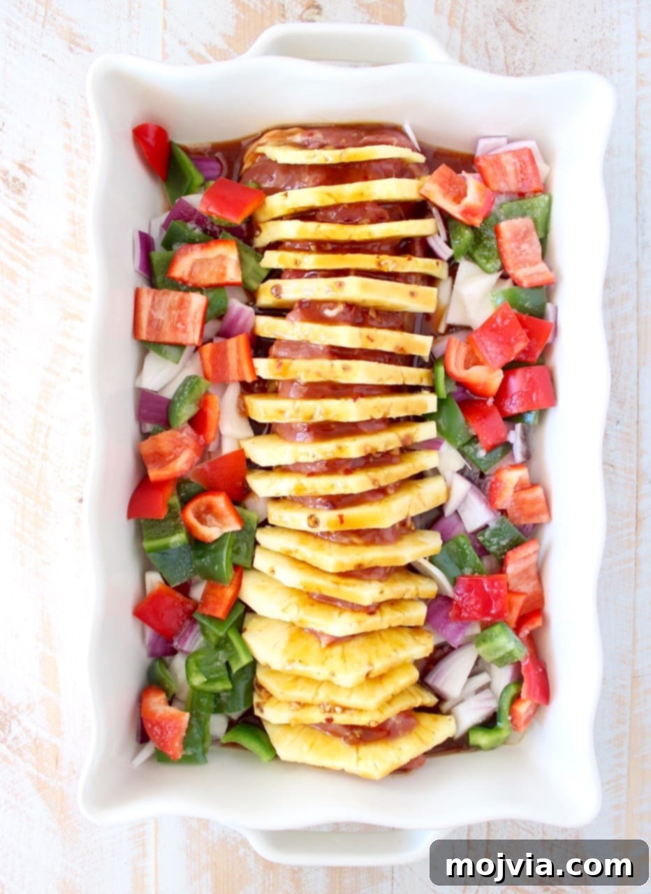 Sweet and Tangy Pineapple Teriyaki Pork Tenderloin 3 uncooked pork tenderloin filled with slices of pineapple in a baking dish surrounded by diced bell peppers and onions