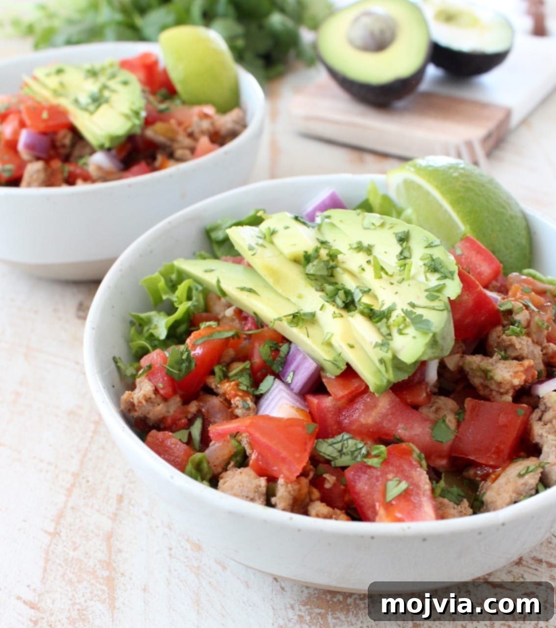Whole30 Power Turkey Taco Salad 2 A beautifully arranged white bowl featuring avocado, taco seasoned ground turkey cooked with peppers, onions and tomatoes, all layered on a bed of fresh lettuce.