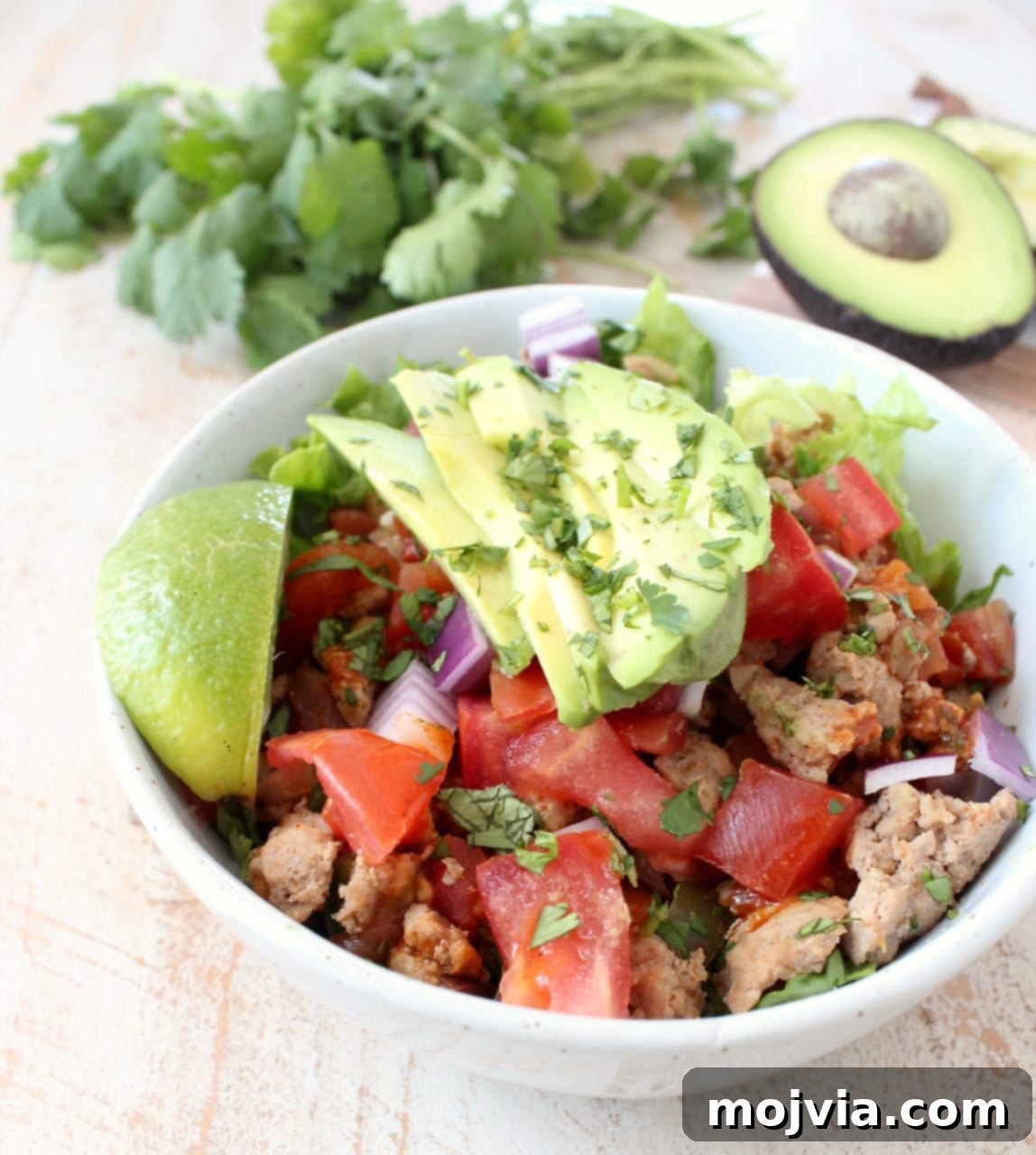 Whole30 Power Turkey Taco Salad 4 A close-up view of a white bowl overflowing with vibrant taco seasoned ground turkey, peppers, onions, and tomatoes, all topping a bed of fresh, crisp lettuce, ready to be enjoyed.