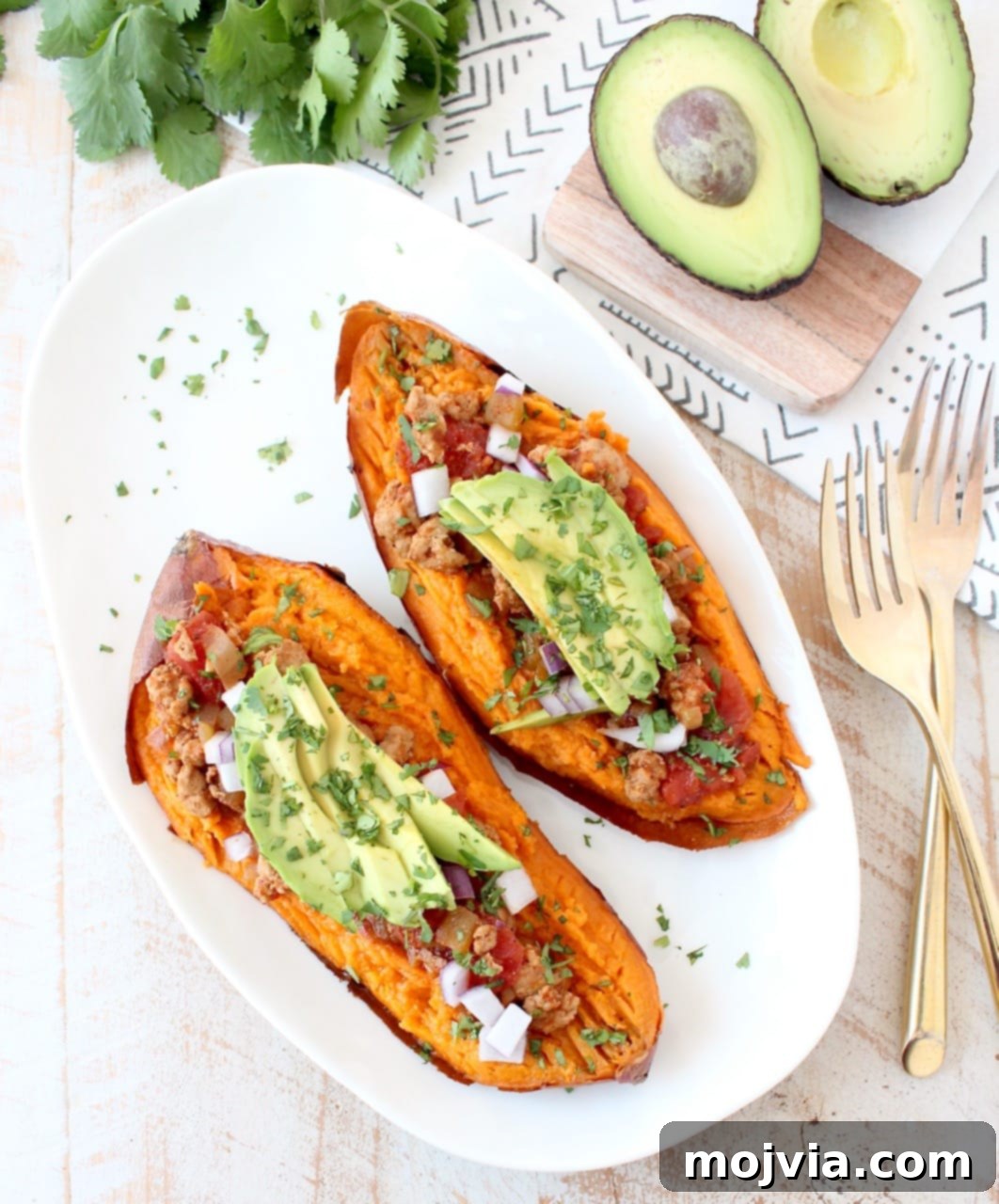 Baked sweet potato cut in half and topped with smoky chipotle chili and sliced avocado on a white plate, showcasing a healthy and vibrant meal.