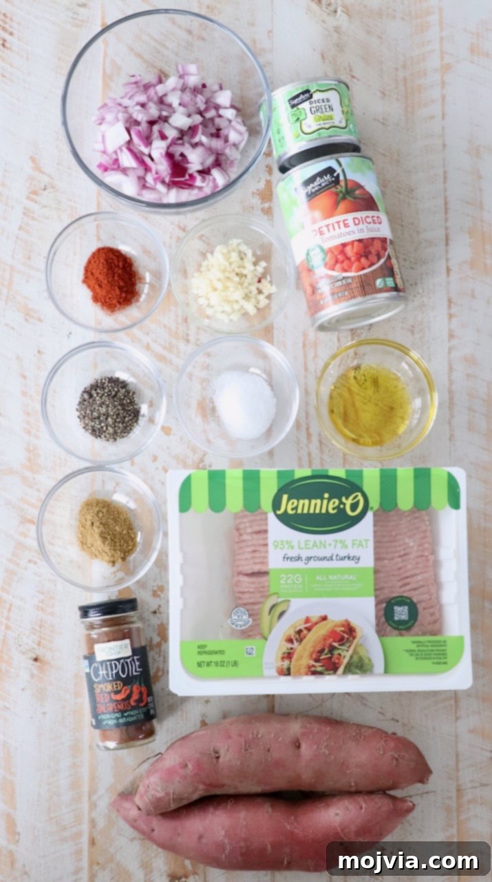 Ingredients for chili stuffed sweet potatoes laid out on a white wooden board, including sweet potatoes, ground turkey, onions, garlic, and spices.