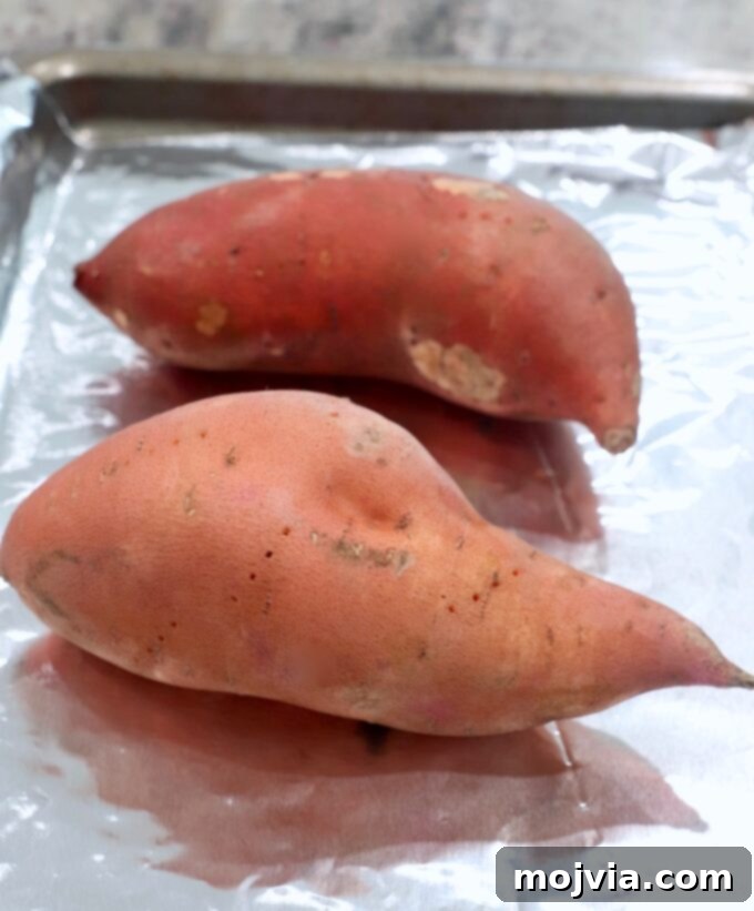 Sweet potatoes ready for baking on a foil-lined baking sheet.
