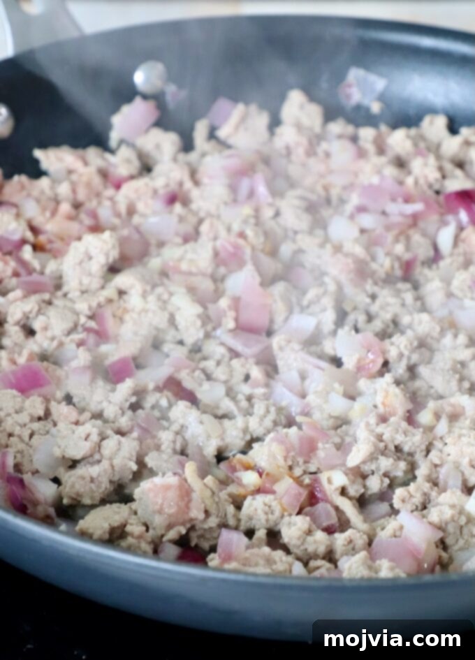 Cooked ground turkey in a skillet with sautéed onions and garlic, forming the base of the chili.