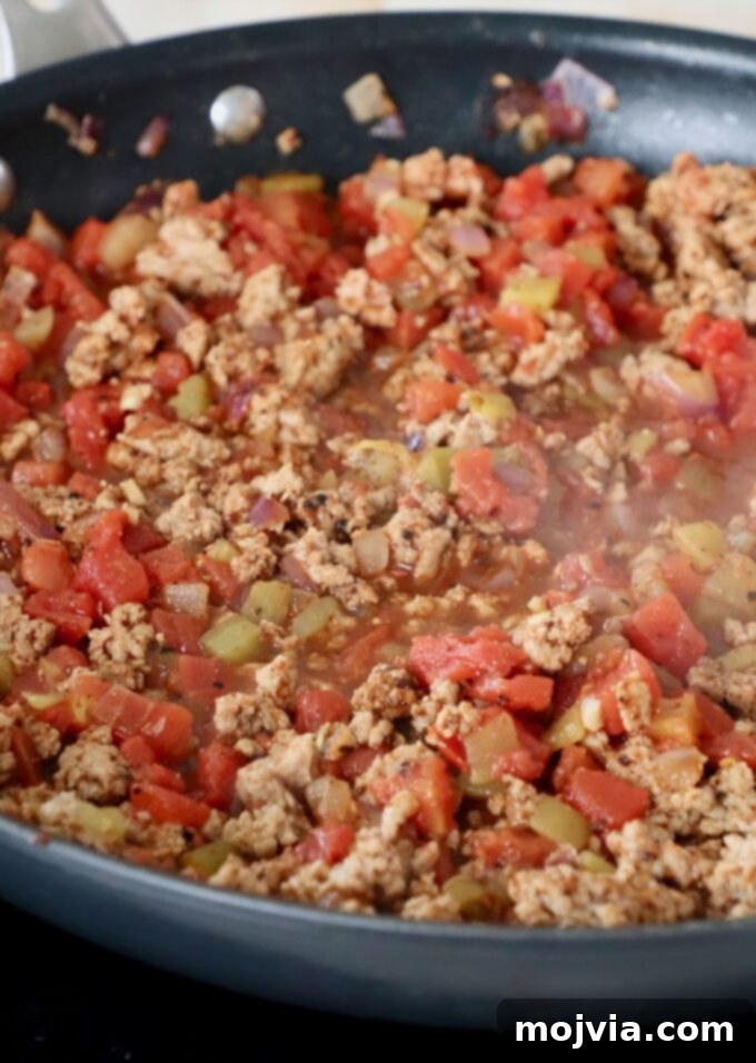 Smoky chipotle chili simmering in a skillet, rich with tomatoes and green chilies.
