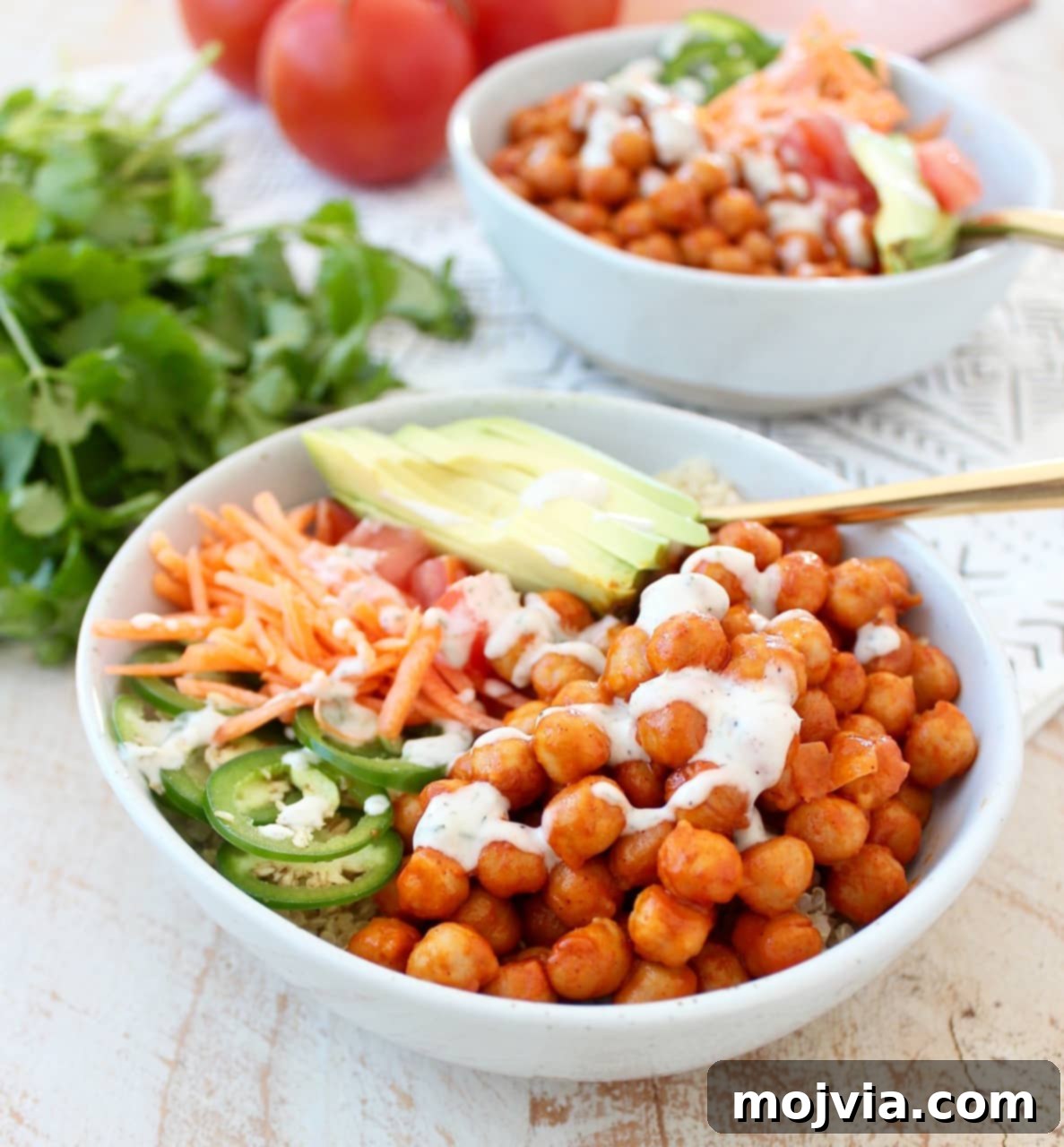 Zesty Buffalo Chickpea Nourish Bowl 2 bowls filled with chickpeas tossed in buffalo sauce and sliced vegetables and a gold fork in the bowl