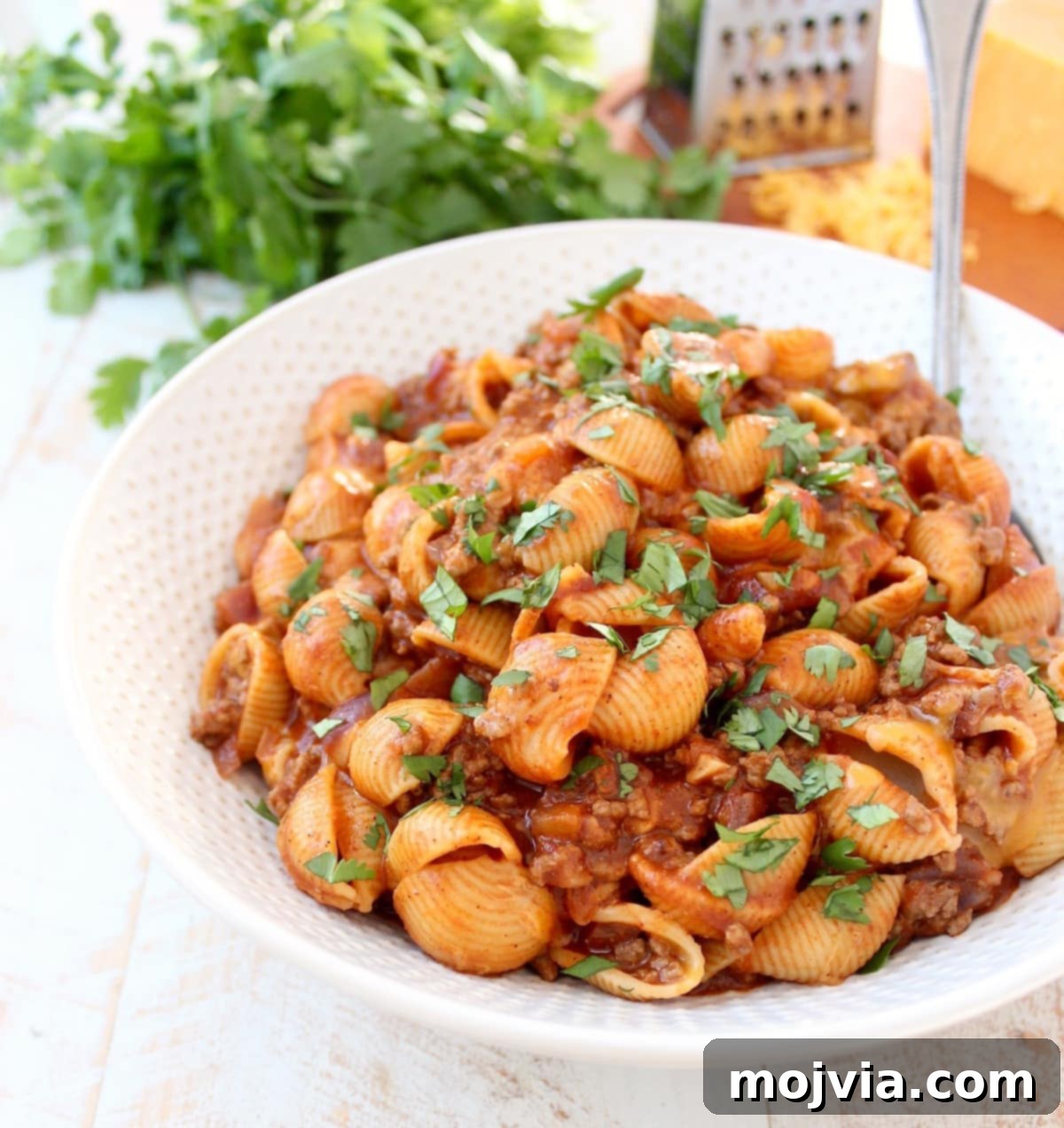 Large bowl of Enchilada Pasta with serving spoon, showing pasta shells, ground beef, and melted cheese
