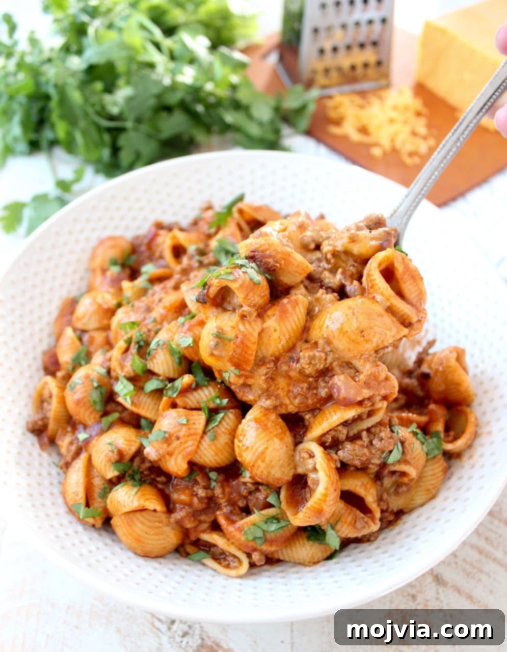 Serving spoon scooping a portion of Enchilada Pasta from a large bowl, showcasing melted cheese and sauce