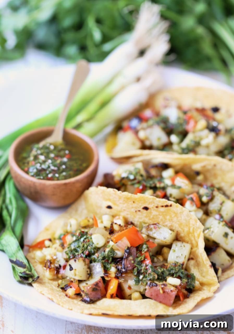 Delicious Vegan Tacos filled with Grilled Potatoes, Peppers, and Corn, topped with fresh Chimichurri Sauce, served on a plate.