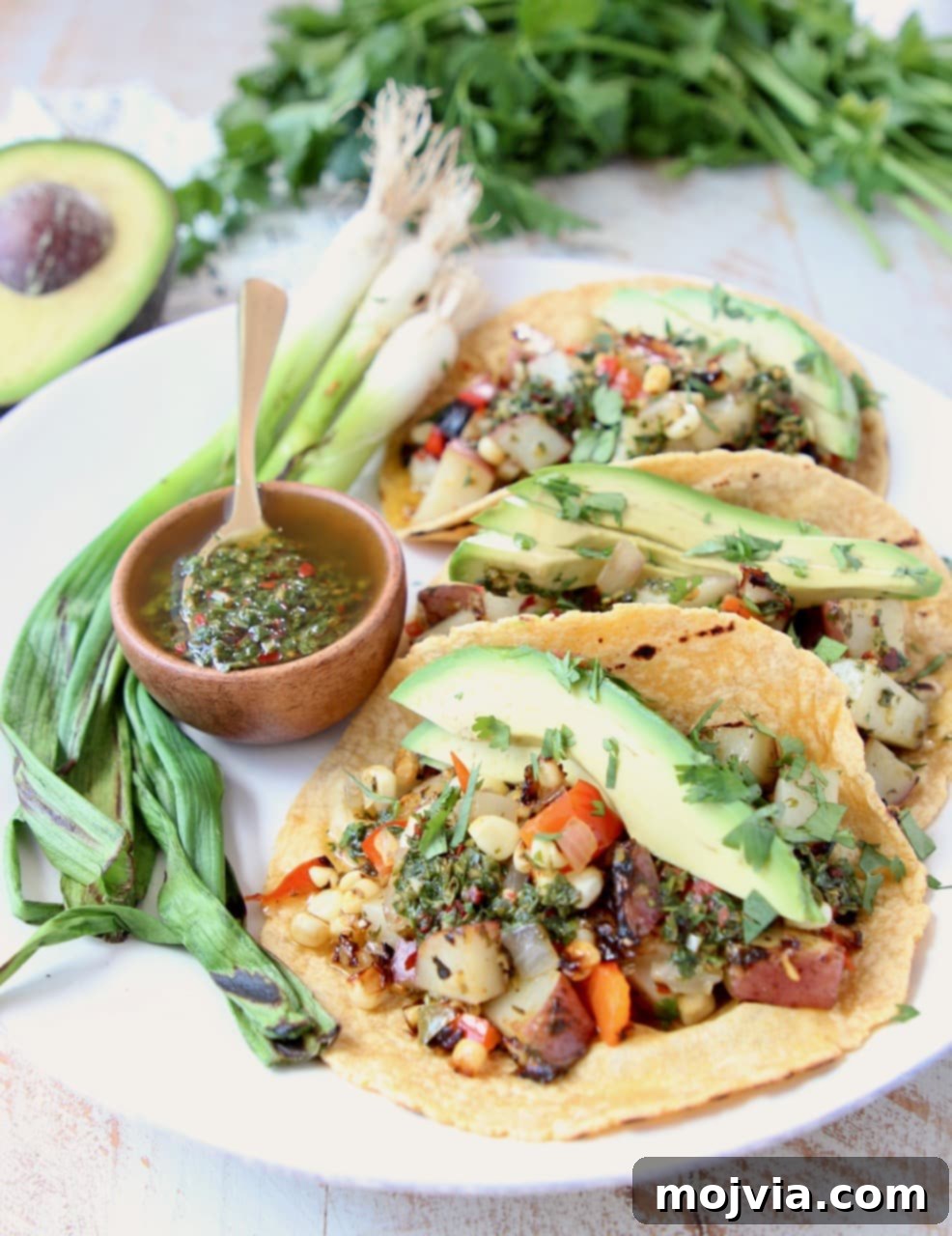 Close-up of a Grilled Vegan Taco, overflowing with tender potatoes, colorful peppers, fresh avocado slices, and a vibrant drizzle of chimichurri sauce.