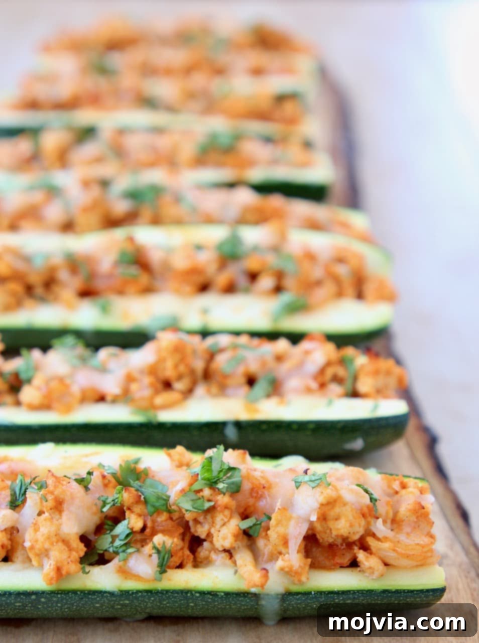 Tangy Buffalo Chicken Zucchini Bake 4 Buffalo Chicken Zucchini Boats on Wood Cutting Board with Fresh Cilantro