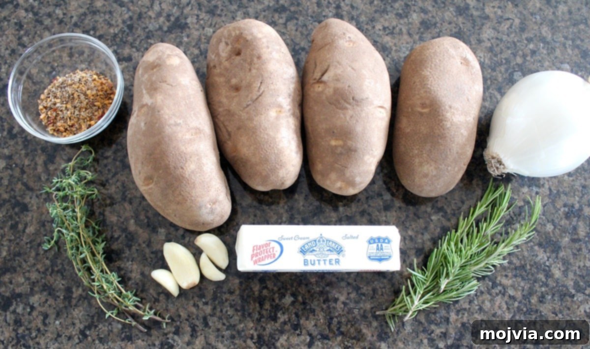 A close-up shot of the fresh ingredients for Cast Iron Skillet Potatoes, including russet potatoes, a white onion, a stick of butter, fresh garlic, and sprigs of thyme and rosemary.
