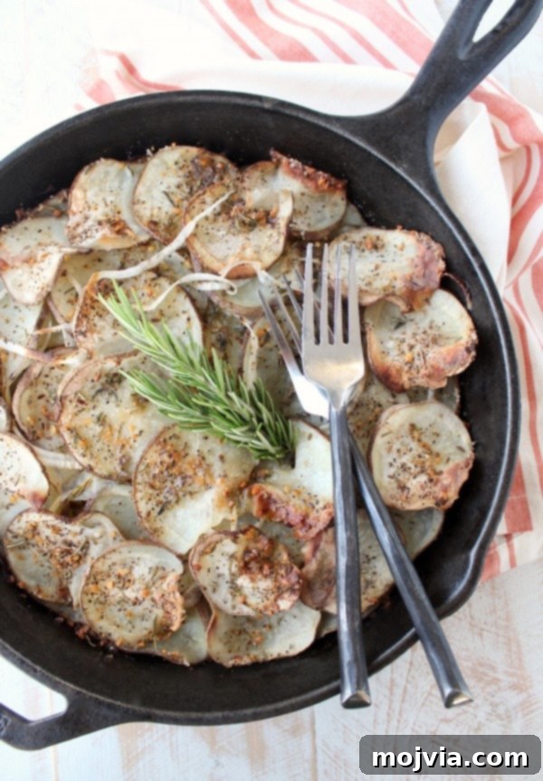 A cast iron skillet filled with perfectly baked, golden-brown sliced potatoes and two forks, inviting diners to share, placed on a rustic wooden table.