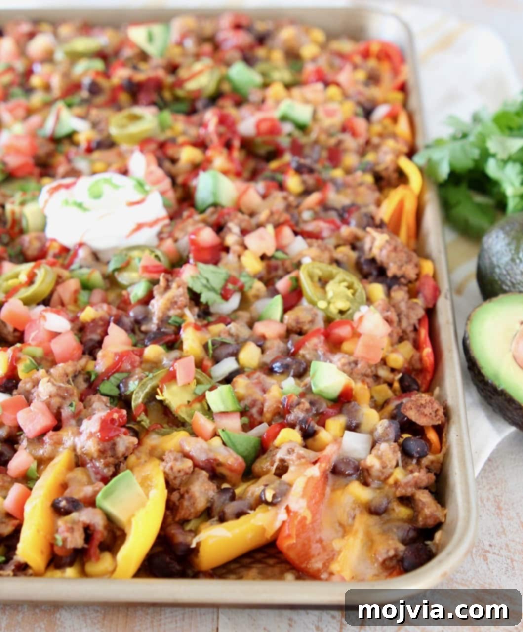 Mini peppers covered in cheese, beans, tomatoes, avocado and cilantro on sheet pan