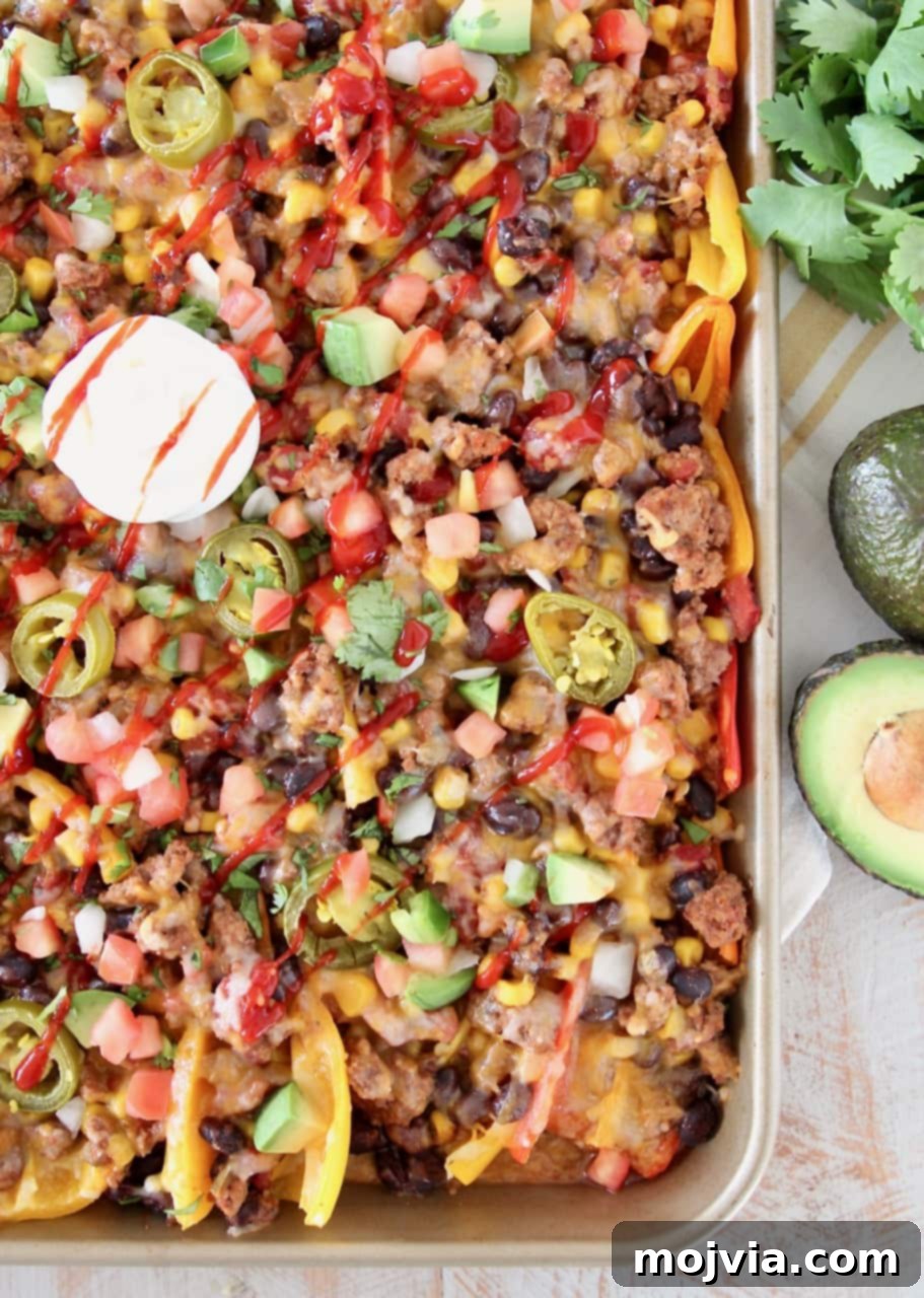 Low Carb Nachos made with sweet mini bell peppers, topped with turkey, beans, corn, tomatoes, jalapenos, avocado, hot sauce and sour cream on a baking sheet