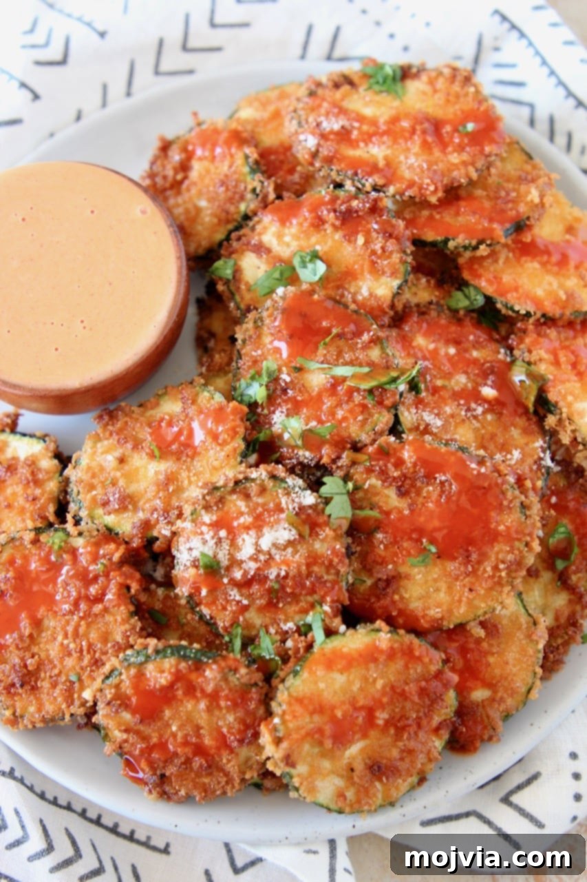 Spicy Buffalo Zucchini Crisps 3 Crispy Zucchini Chips drizzled with buffalo sauce on plate with small bowl of buffalo blue cheese dressing