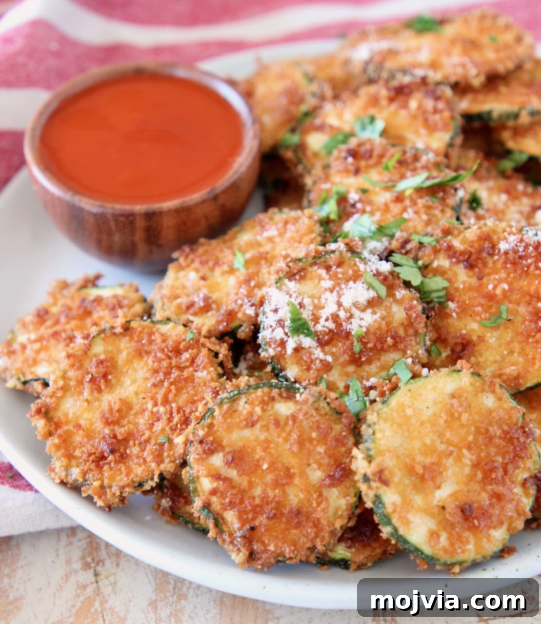 Spicy Buffalo Zucchini Crisps 4 Crispy fried zucchini chips with parmesan cheese on a plate with small wooden bowl of buffalo sauce