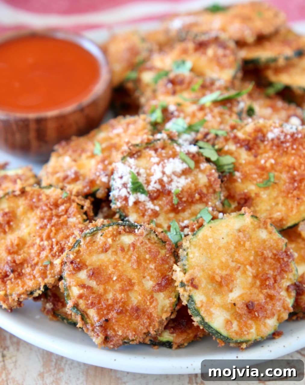 Spicy Buffalo Zucchini Crisps 5 Crispy zucchini chips with parmesan cheese on plate with small bowl of buffalo sauce