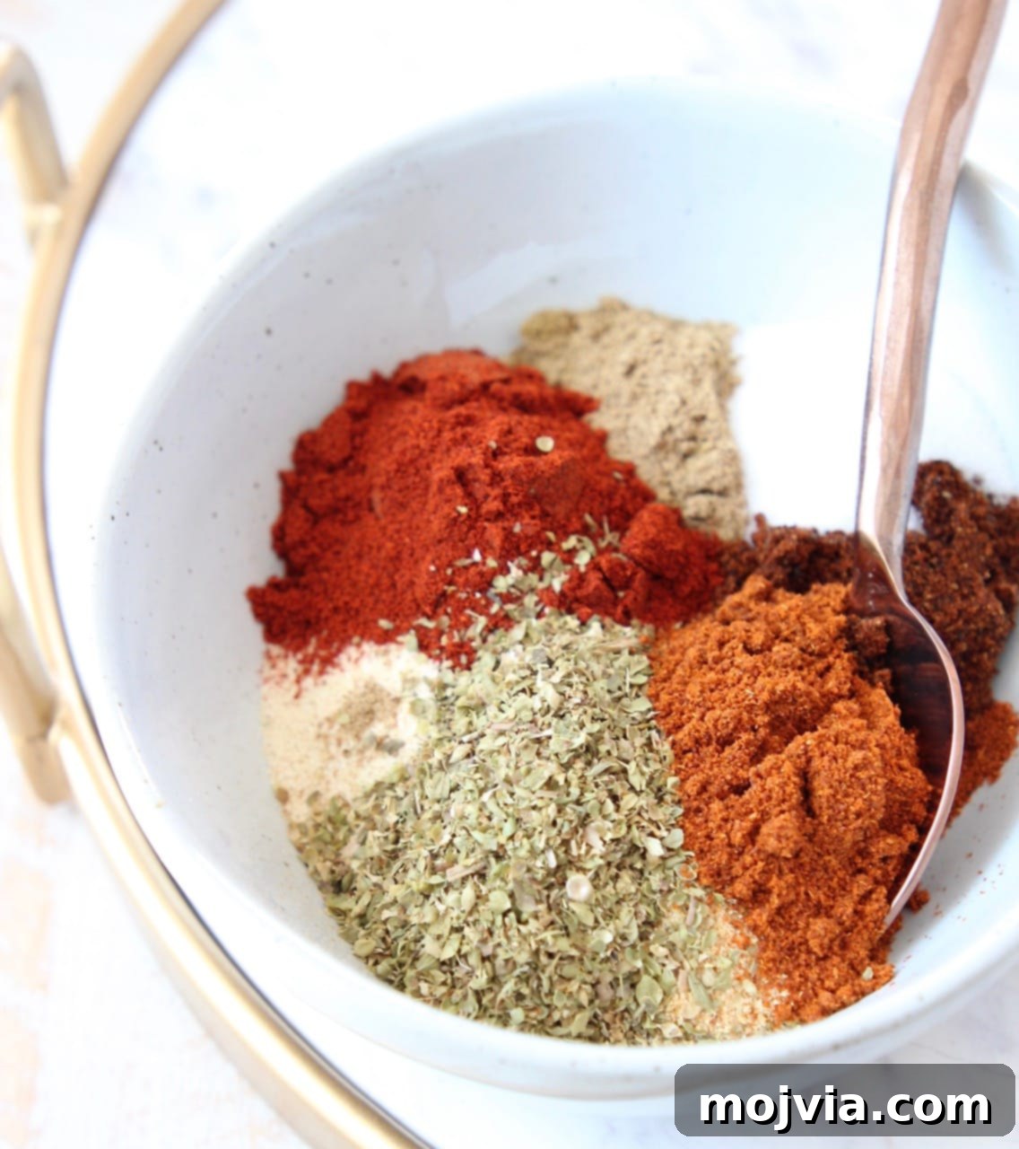 dried herbs and spices separated in bowl with spoon, ready to be mixed into homemade taco seasoning