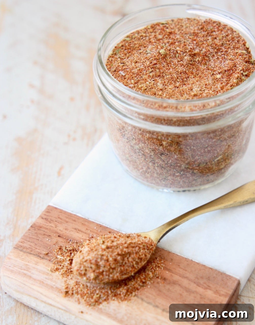 taco seasoning stored in a mason jar on a marble cutting board with a spoon showing the mixed spices