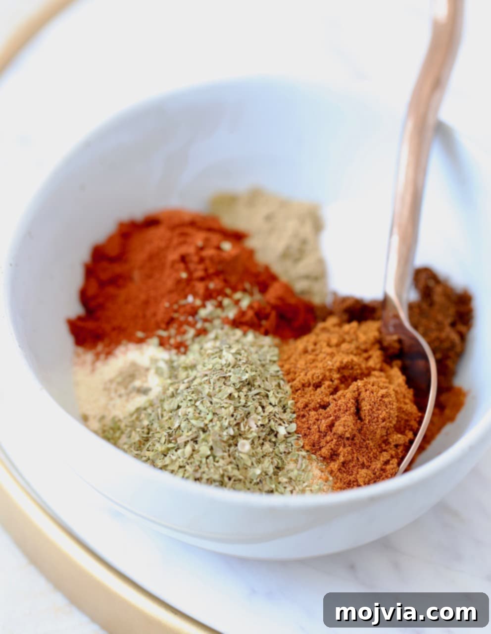 Homemade taco seasoning with 8 different spices separated in a bowl with a spoon
