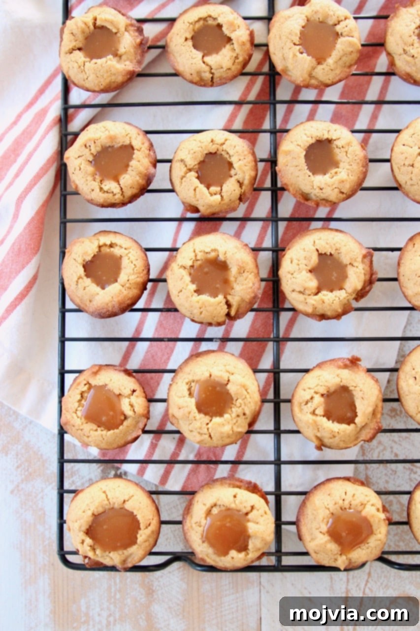 Pumpkin cookie cups filled with salted caramel on black wire baking rack with orange striped towel