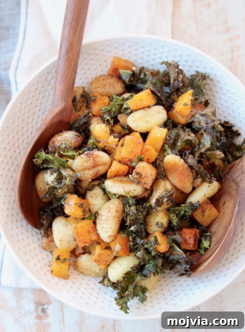 Close-up of a serving of Sheet Pan Gnocchi, butternut squash, and crispy kale in a large white bowl with wooden serving spoons.