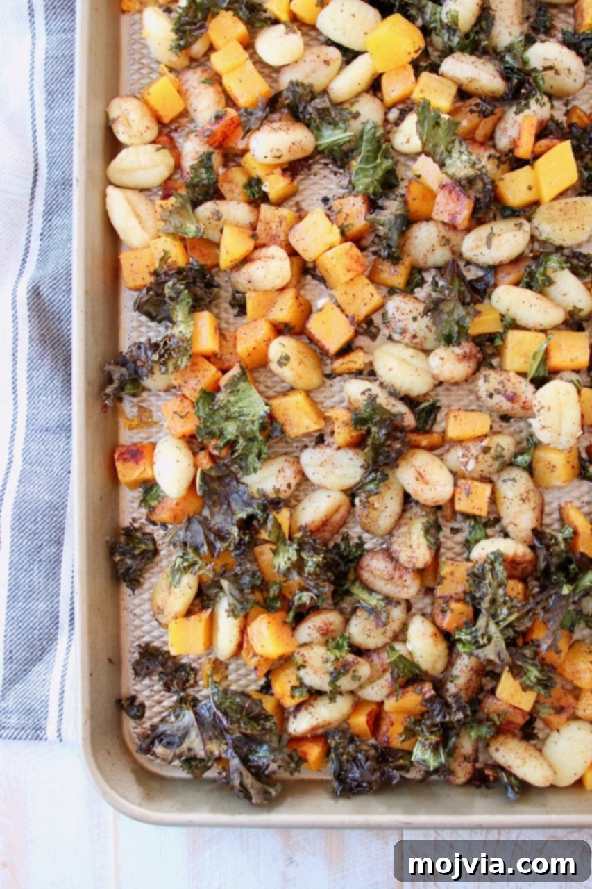 Sheet Pan Gnocchi with butternut squash and kale, fresh out of the oven on a baking sheet, with a grey striped towel nearby.