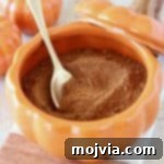 Homemade pumpkin pie spice in a pumpkin bowl with a small gold spoon on small marble and wood cutting board