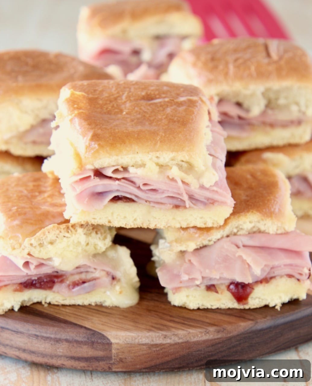 Sweet & Savory Cranberry Brie Ham Sliders 3 Stacked Cranberry Brie Ham Sliders on Hawaiian rolls, ready to be served on a stylish wooden cutting board.