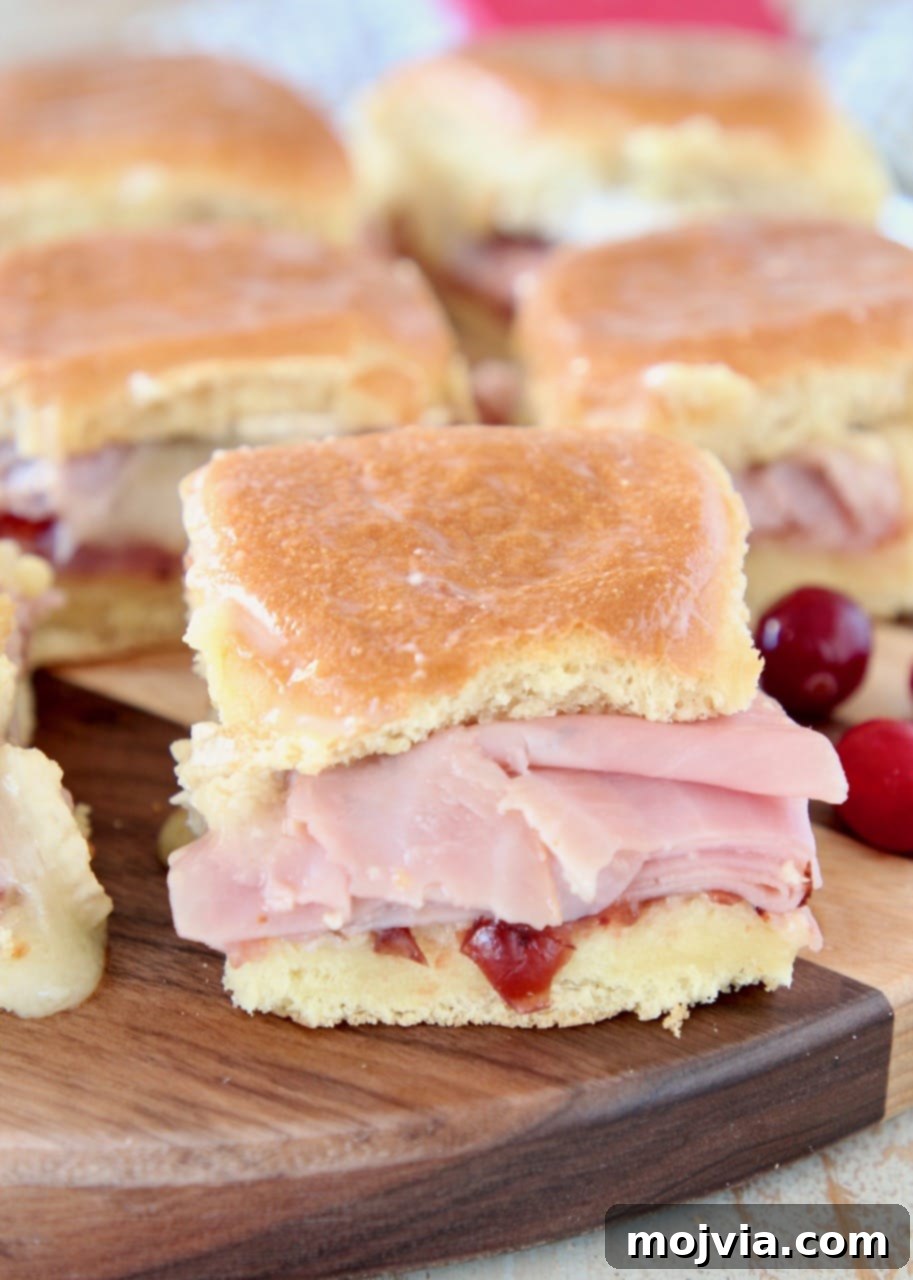 Sweet & Savory Cranberry Brie Ham Sliders 5 A festive arrangement of Cranberry Brie Ham Sliders on Hawaiian rolls, garnished with fresh cranberries on a wooden serving board.