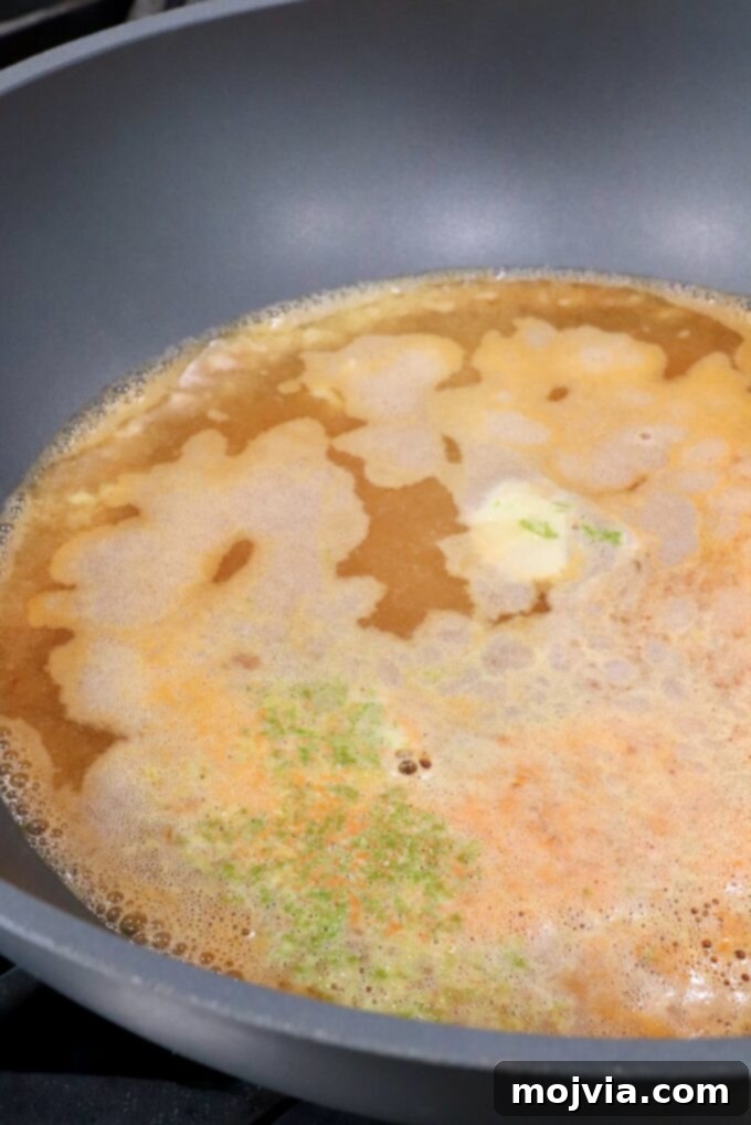 A large pot on the stove, gently simmering a fragrant broth infused with lime zest, whole garlic cloves, and a piece of ginger, creating an aromatic base for the soup.